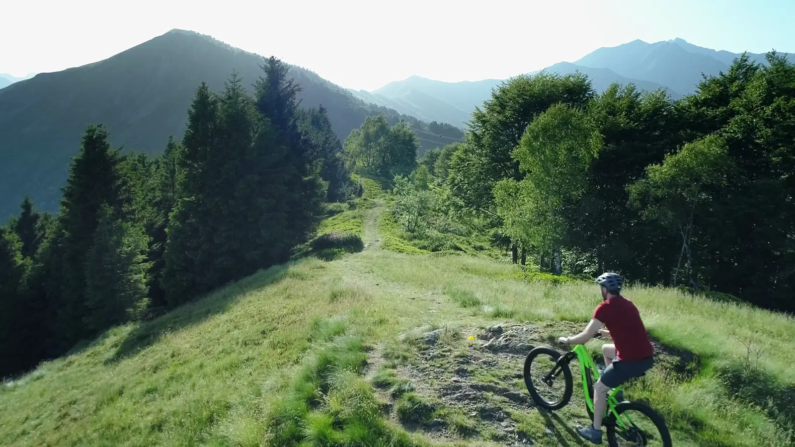 Mountainbiker im roten Trikot auf einem Gratweg zwischen Wald und Bergen